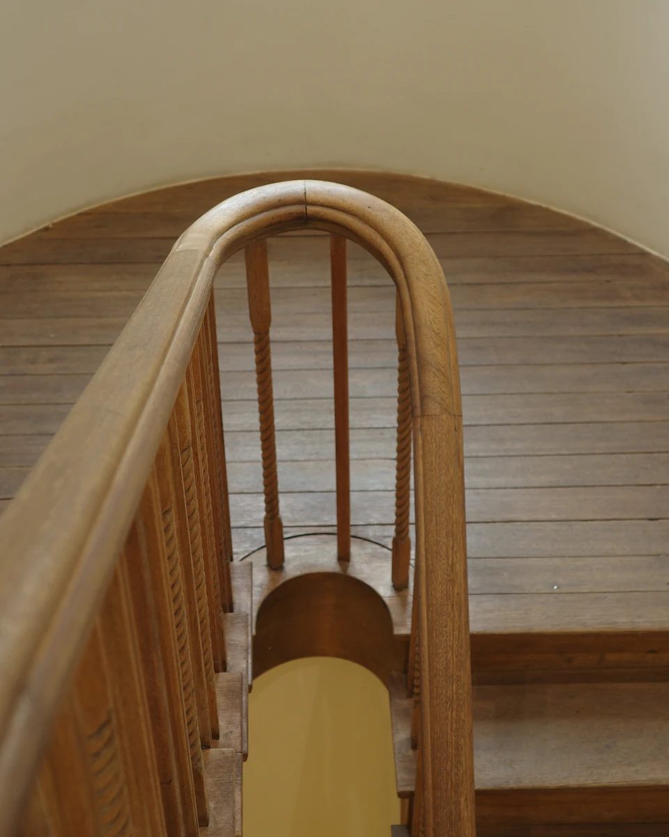 Curving timber staircase and crafted handrail against pale architectural walls; illustrative interior, not a managed-property portfolio