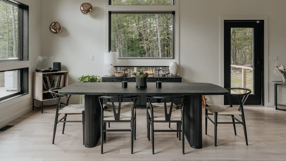Dark fluted dining table, woven chairs and large woodland-facing windows; illustrative interior, not a managed-property portfolio